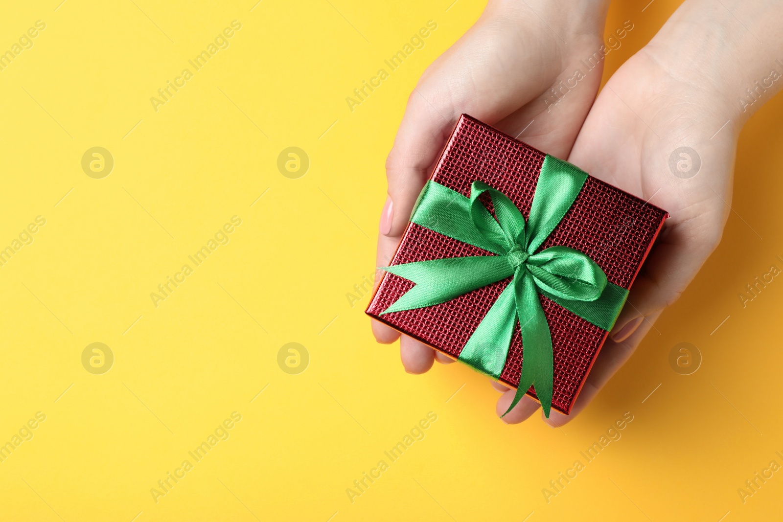 Photo of Woman holding beautifully wrapped Christmas gift box on yellow background, top view. Space for text