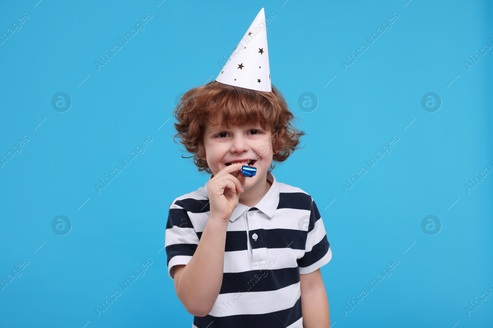 Photo of Cute little boy in party hat with blower on light blue background