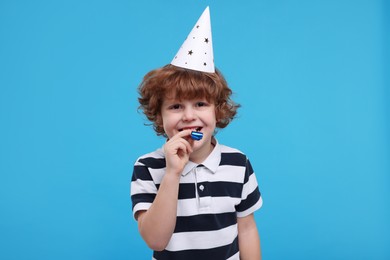 Cute little boy in party hat with blower on light blue background