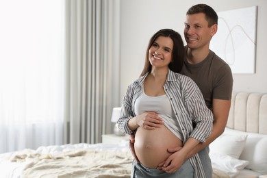 Photo of Young pregnant woman with her husband in bedroom