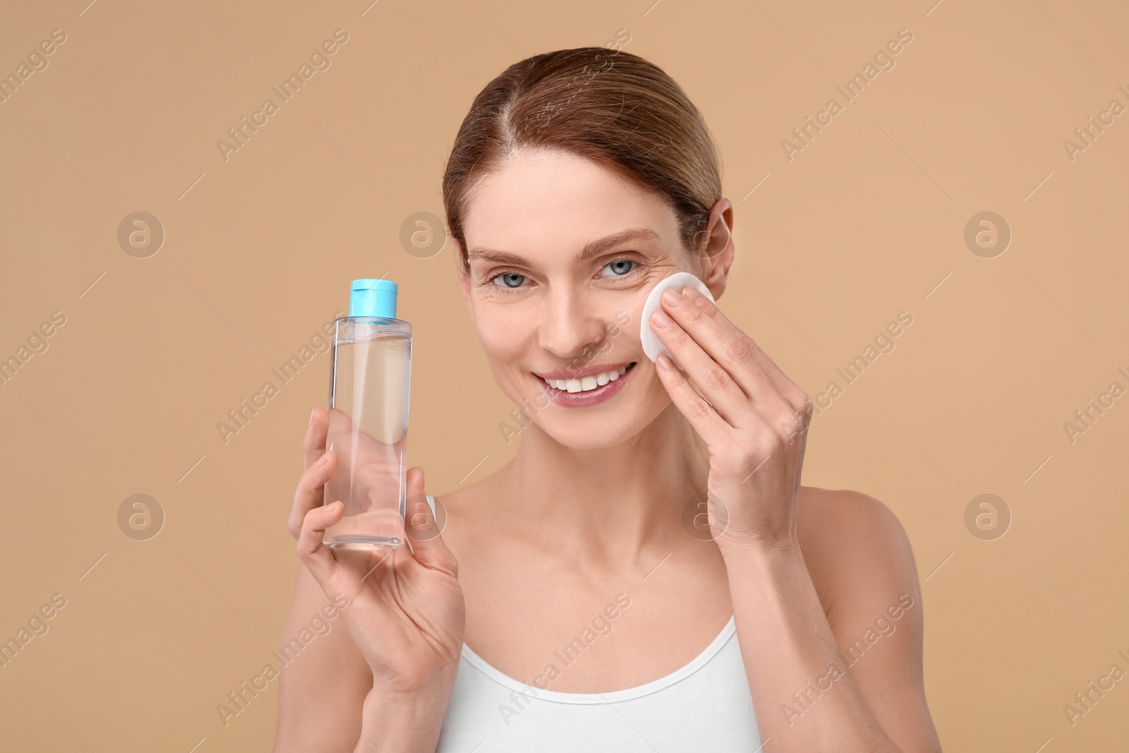 Photo of Beautiful woman removing makeup with cotton pad on beige background