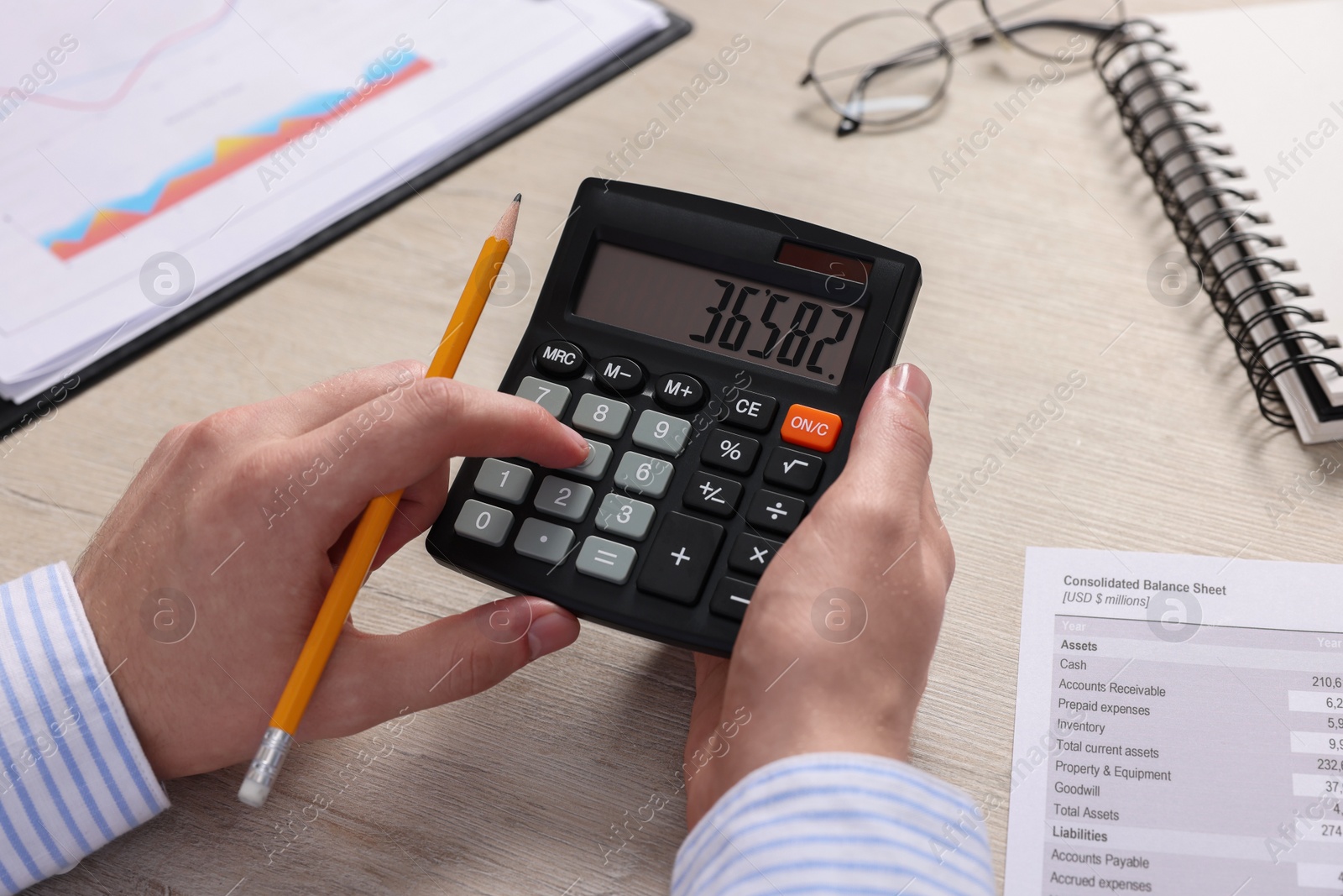 Photo of Man using calculator at wooden table, closeup