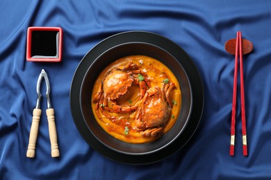 Delicious boiled crabs with sauce served on blue tablecloth, flat lay