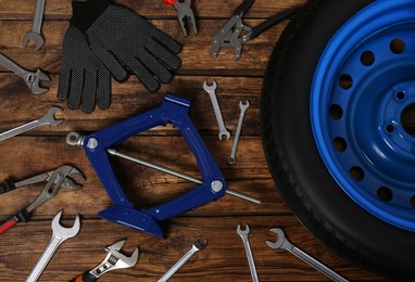 Car wheel, scissor jack, gloves and different tools on wooden surface, flat lay