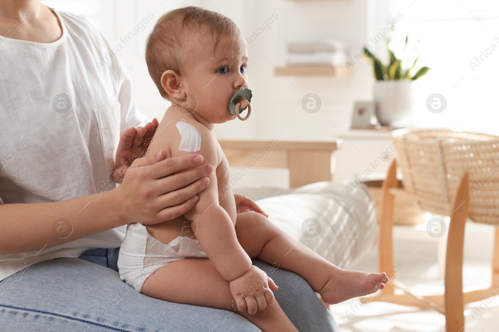 Photo of Mother applying body cream on her little baby at home, closeup