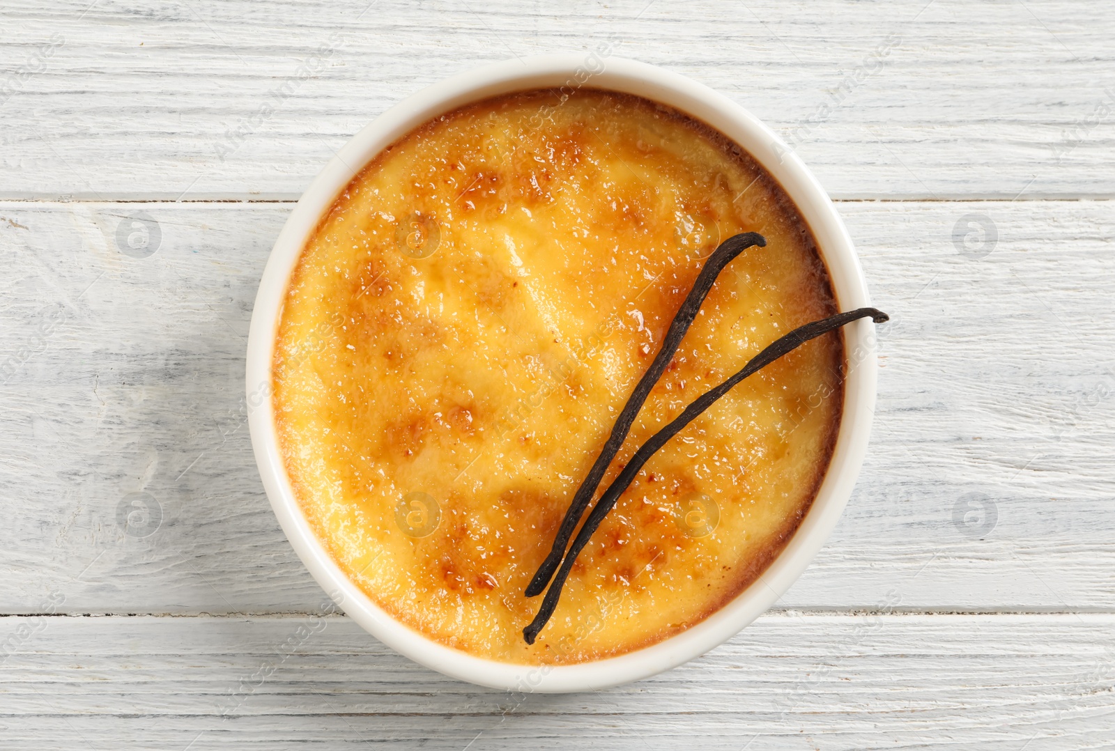 Photo of Delicious creme brulee and vanilla sticks on white wooden table, top view