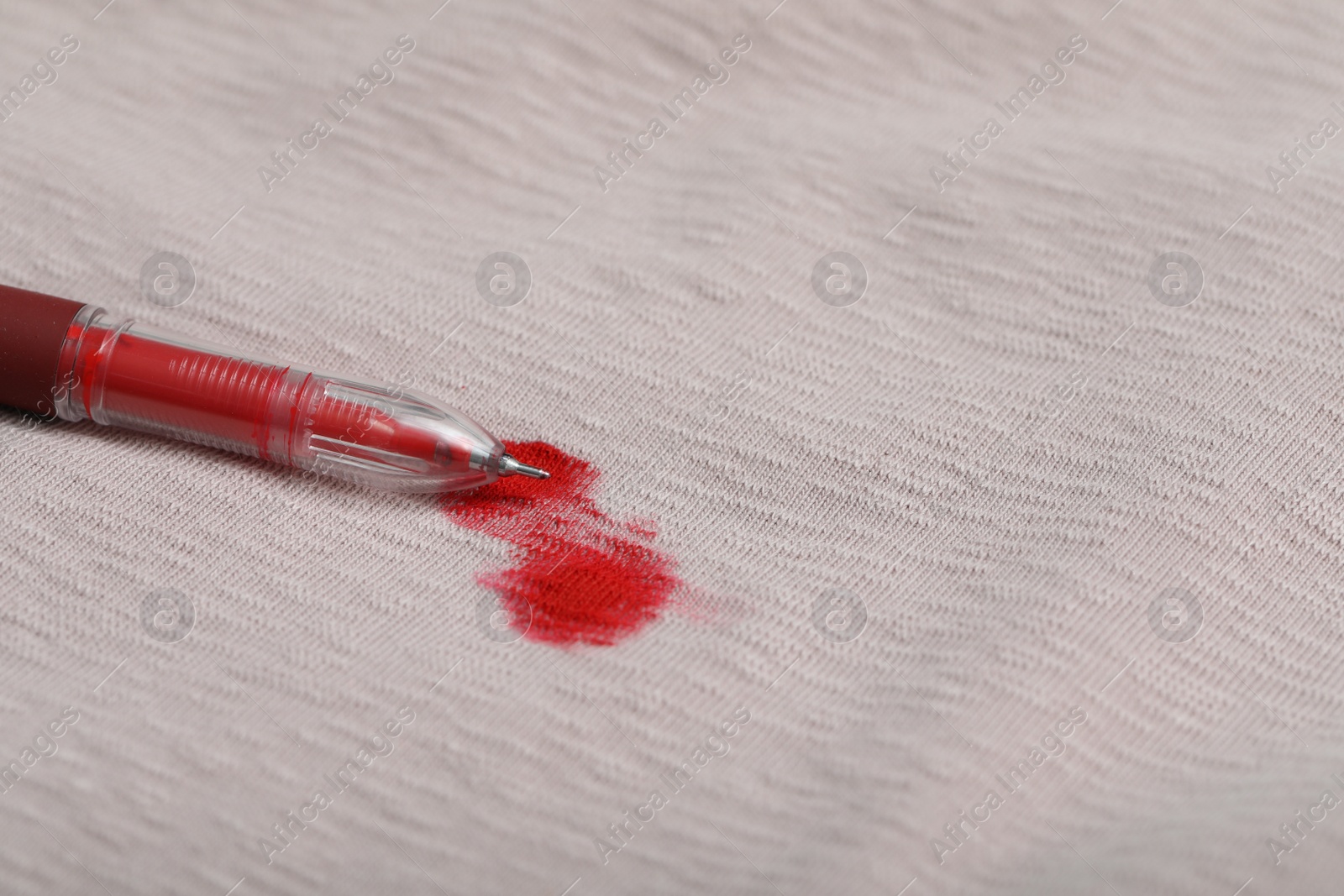 Photo of Pen and stain of red ink on beige shirt, closeup. Space for text