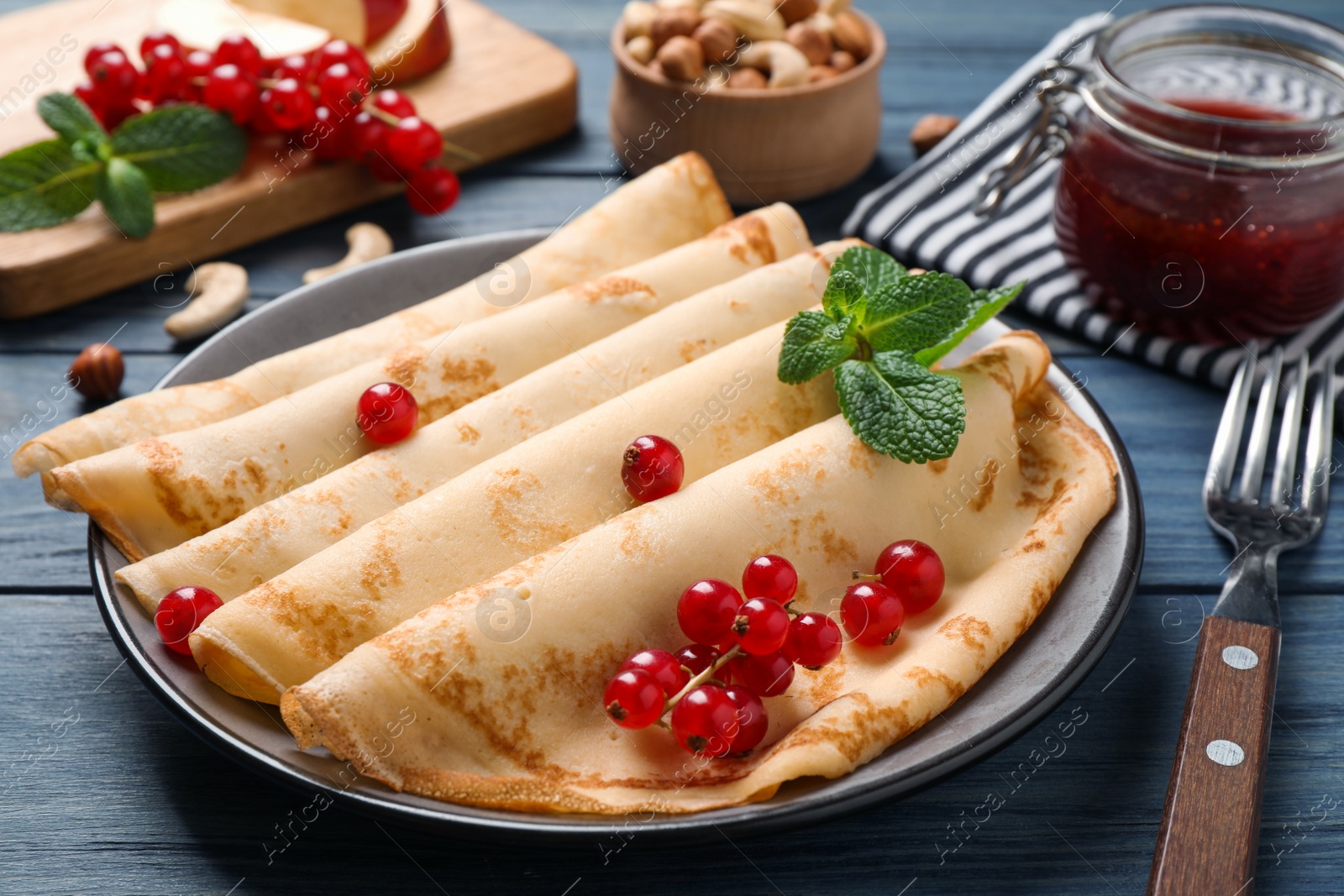 Photo of Delicious thin pancakes with berries on blue wooden table