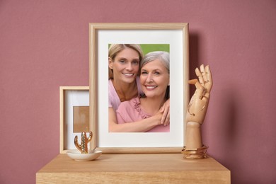 Family portrait of mother and daughter in photo frame on table near color wall