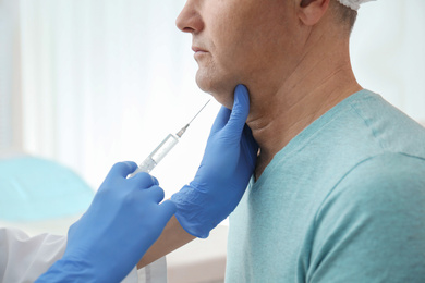 Photo of Mature man with double chin receiving injection in clinic, closeup