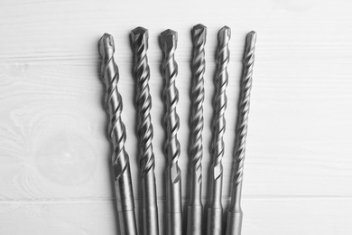 Photo of Different drill bits on white wooden table, flat lay