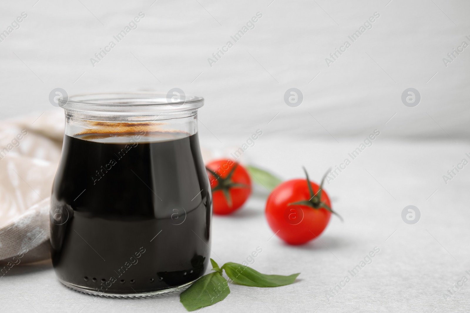 Photo of Glass jar with balsamic vinegar, basil and tomatoes on white table, closeup. Space for text