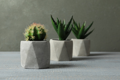 Photo of Artificial plants in ceramic flower pots on grey wooden table