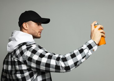 Handsome man holding orange can of spray paint on grey background