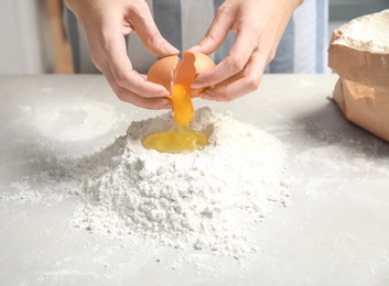 Photo of Woman breaking egg over pile of flour on table in kitchen