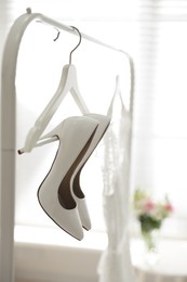 Photo of Pair of white high heel shoes and wedding dress on clothing rack indoors