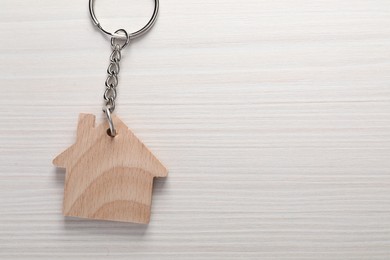 Photo of One keychain in shape of house on light wooden table, top view. Space for text