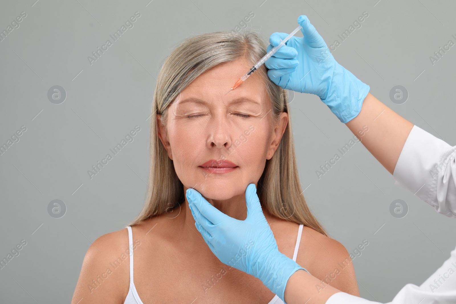 Photo of Doctor giving facial injection to senior woman on light grey background, closeup. Cosmetic surgery