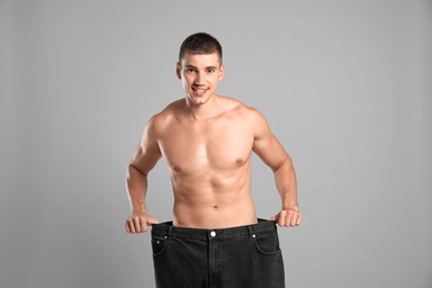 Young man with slim body in old big size jeans on grey background