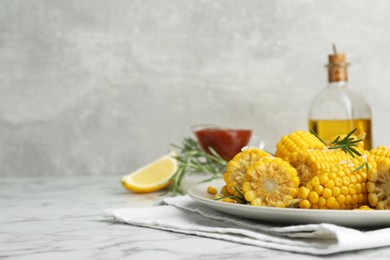 Photo of Plate with tasty cooked corn cobs on white marble table, space for text