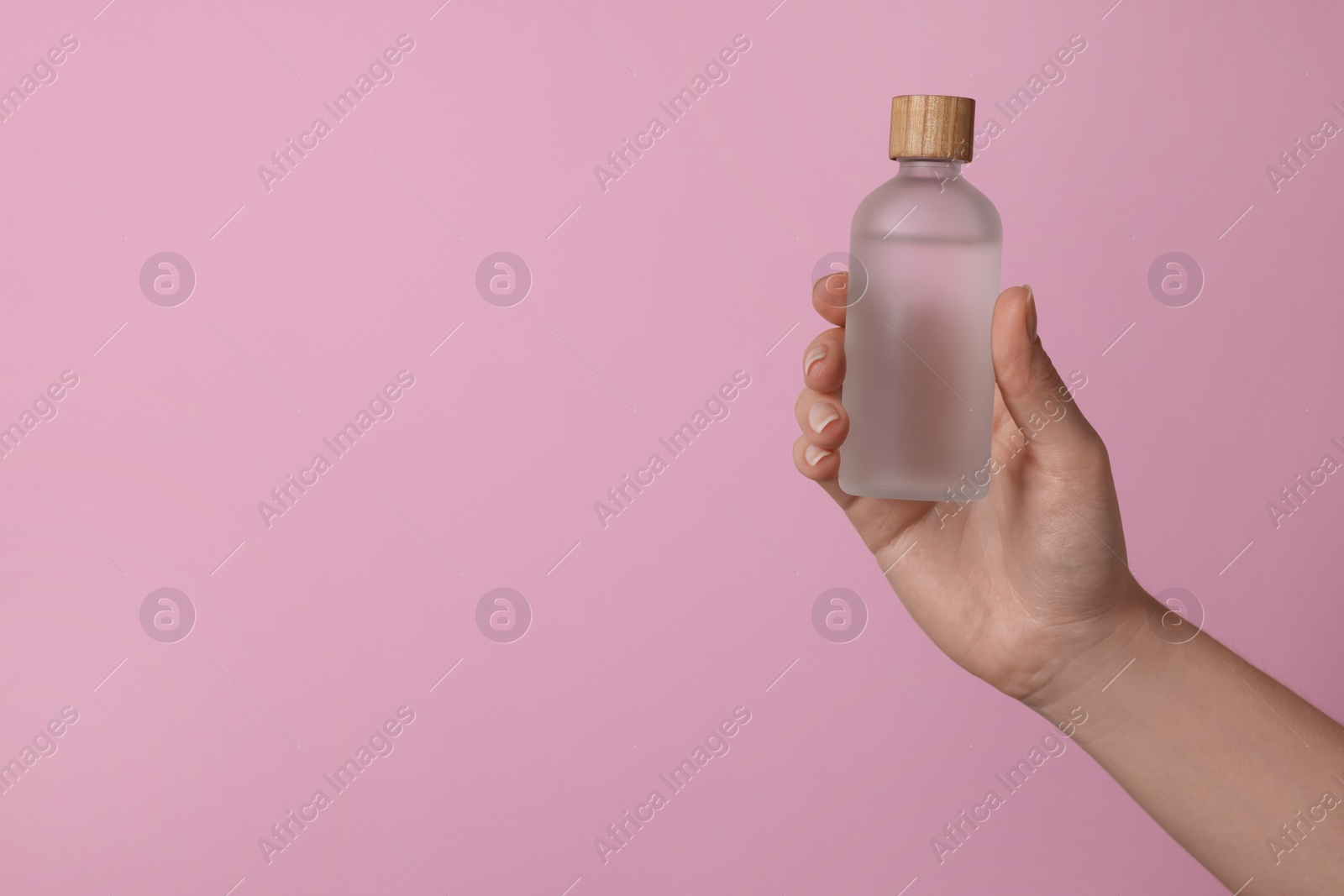 Photo of Woman holding bottle of cosmetic product on pink background, closeup. Space for text