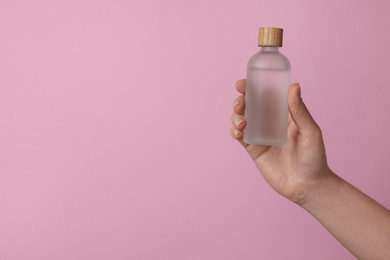 Woman holding bottle of cosmetic product on pink background, closeup. Space for text