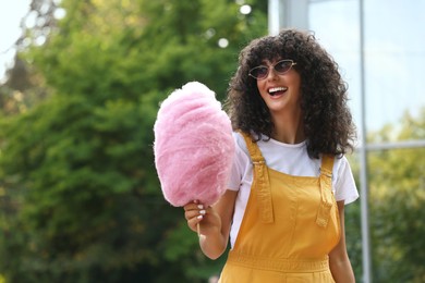 Photo of Smiling woman with cotton candy outdoors. Space for text