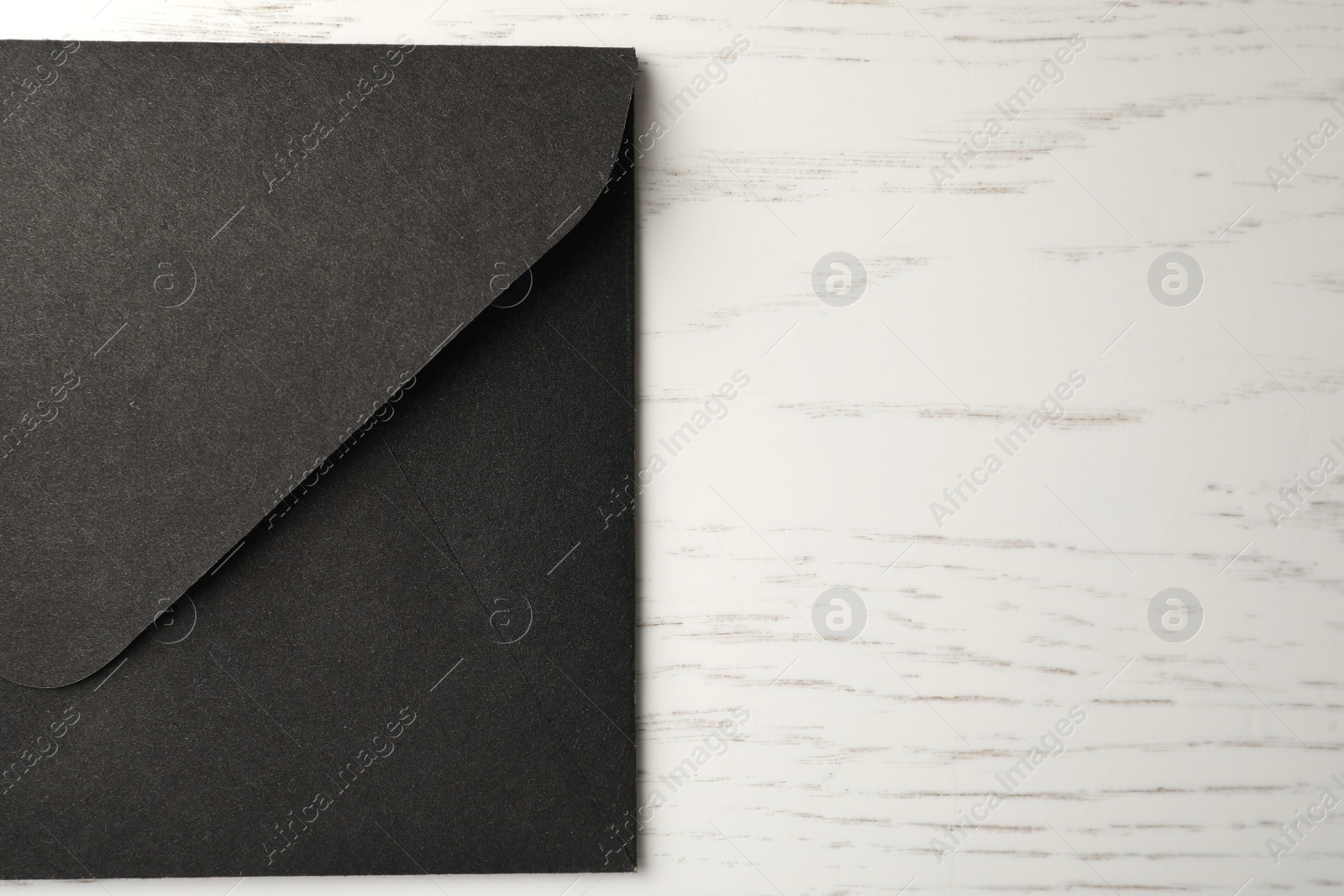 Photo of Black paper envelope on white wooden background, top view. Space for text