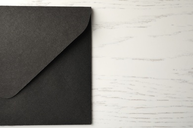 Black paper envelope on white wooden background, top view. Space for text