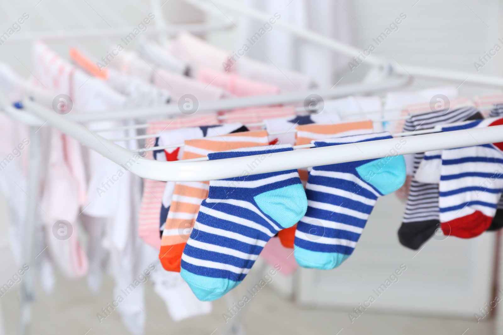 Photo of Different colorful socks on drying rack against blurred background, closeup