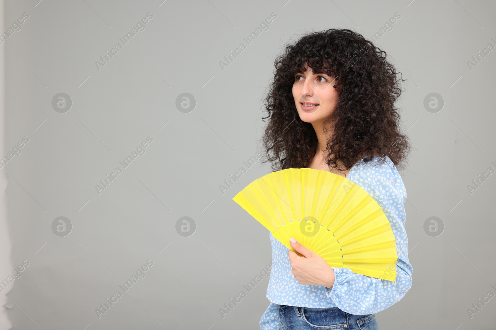 Photo of Happy woman with hand fan suffering from heat on light grey background. Space for text