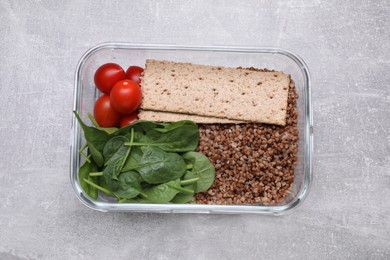 Photo of Glass container with buckwheat, fresh tomato, spinach and crispbreads on light grey table, top view