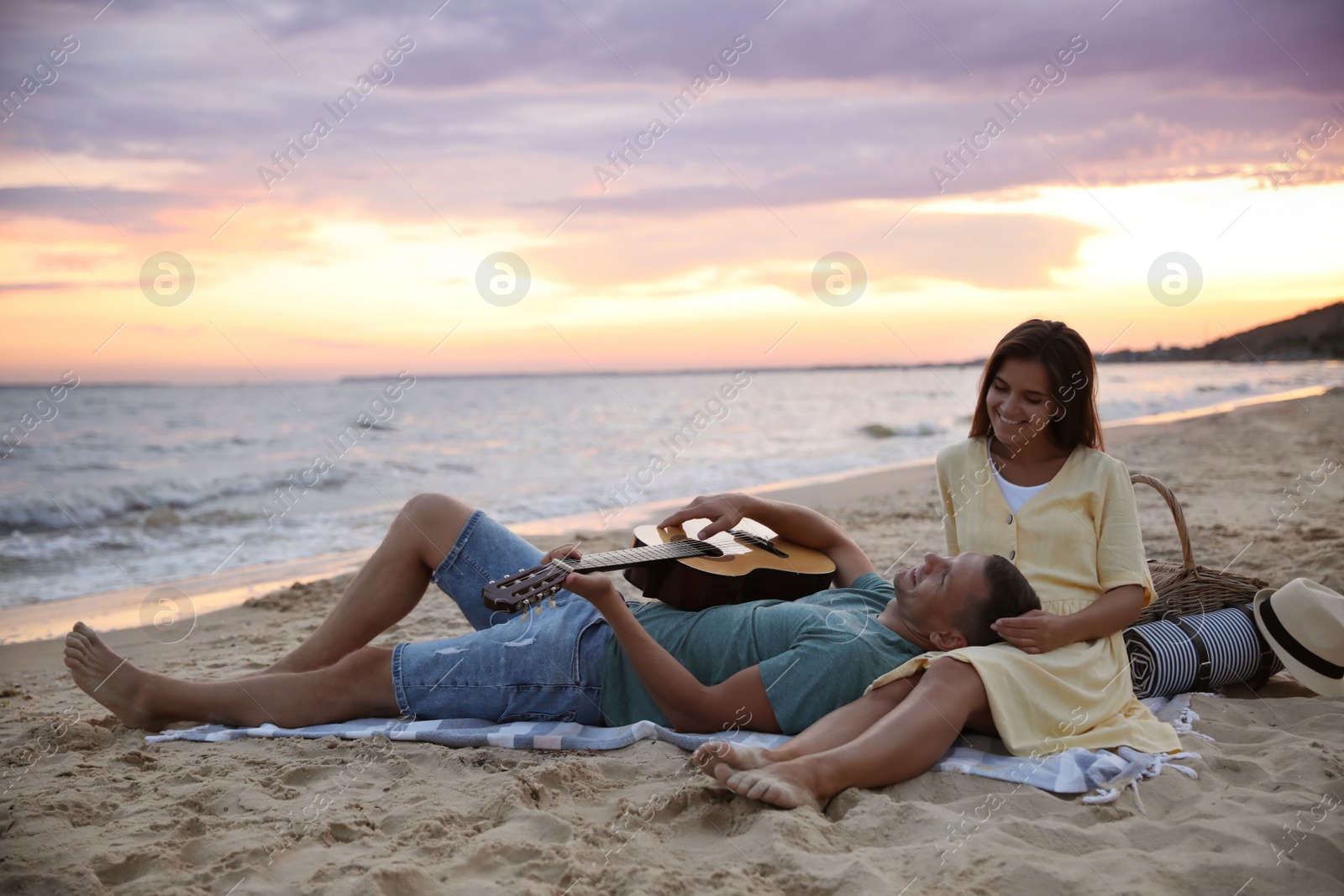 Photo of Lovely couple with guitar and picnic basket on beach at sunset