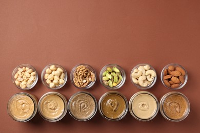 Photo of Many tasty nut butters in jars and nuts on brown table, flat lay. Space for text