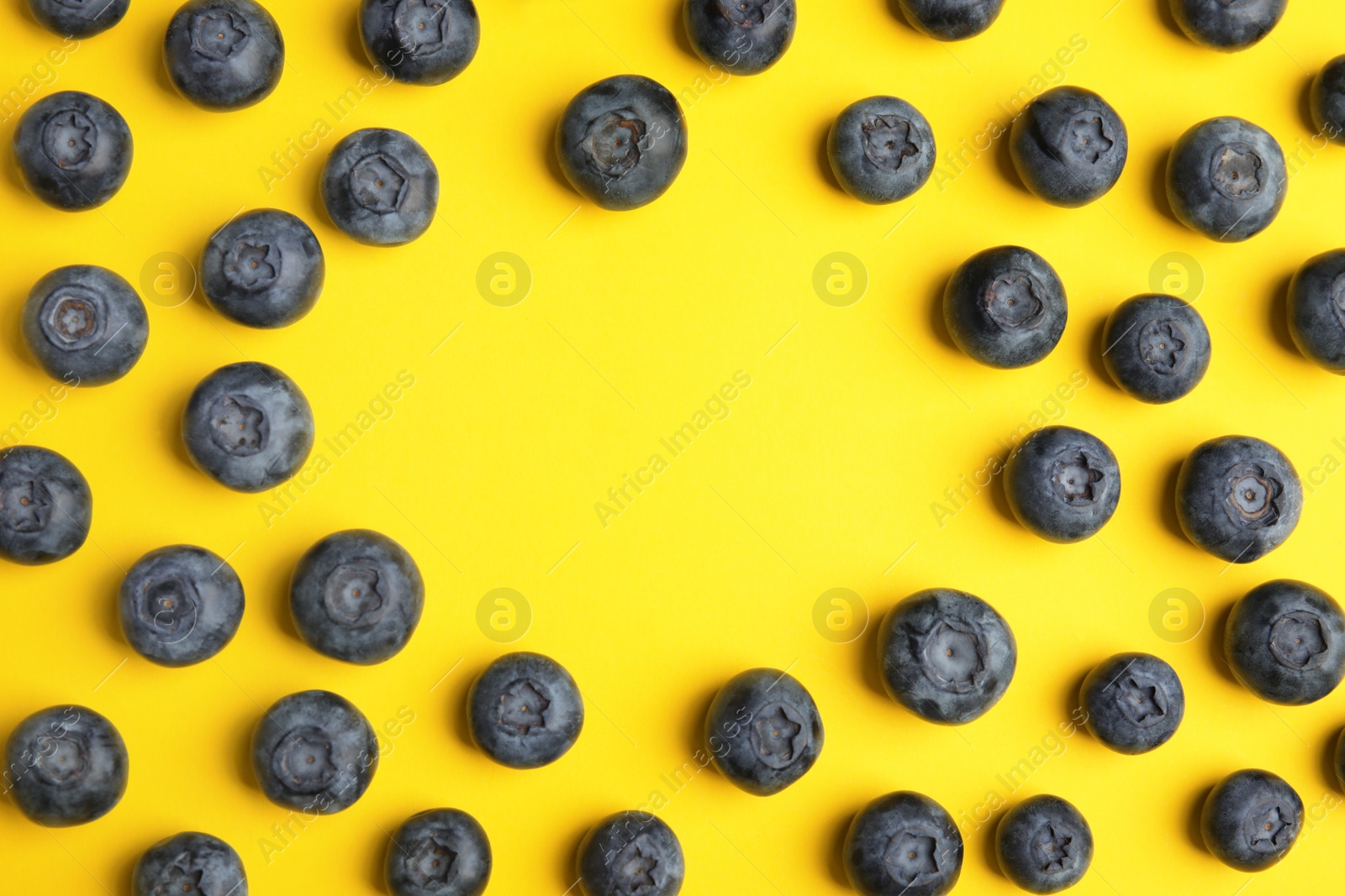 Photo of Frame of ripe blueberries on yellow background, flat lay with space for text