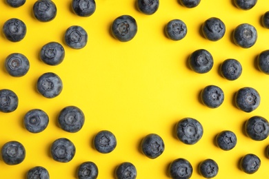 Frame of ripe blueberries on yellow background, flat lay with space for text