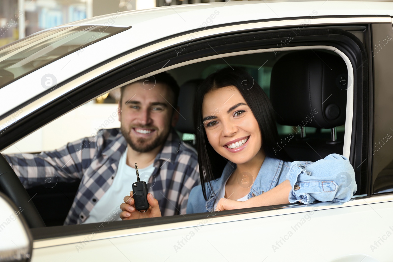 Photo of Happy couple with car key sitting in modern auto at dealership