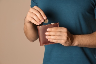 Young man putting coin into wallet on beige background, closeup