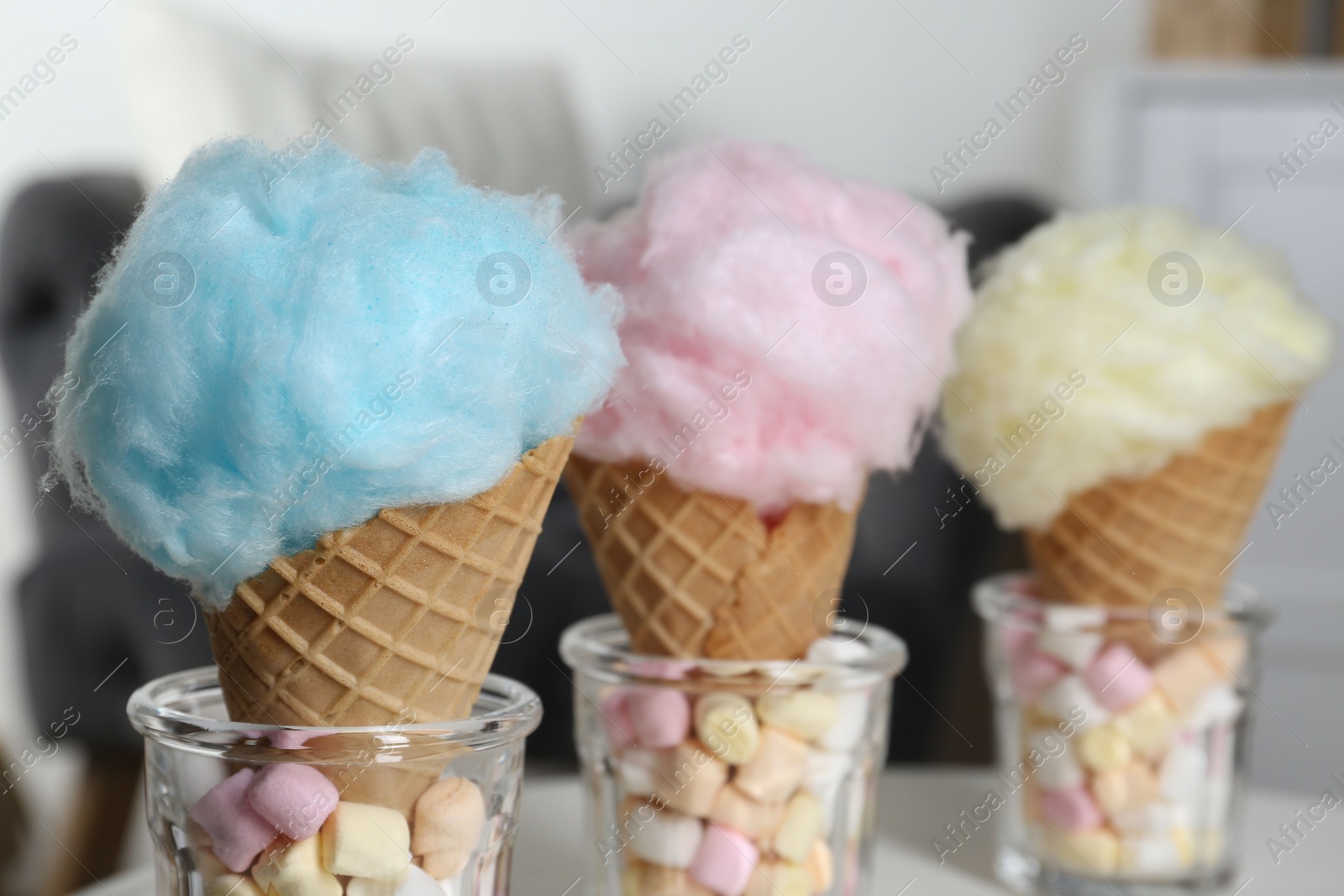 Photo of Sweet cotton candies in waffle cones and marshmallows on blurred background, closeup