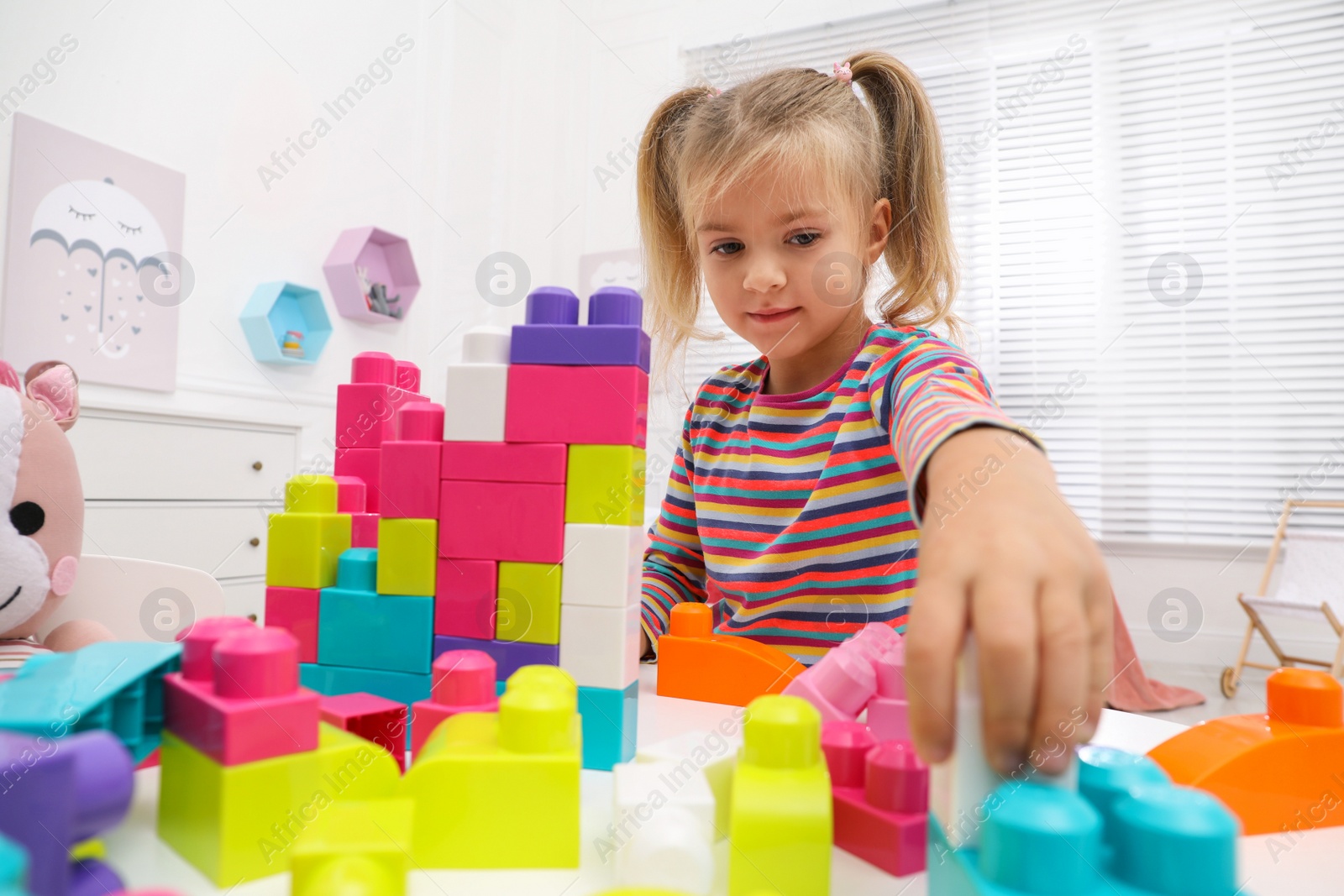 Photo of Cute little girl playing with colorful building blocks at table in room