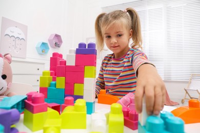 Cute little girl playing with colorful building blocks at table in room