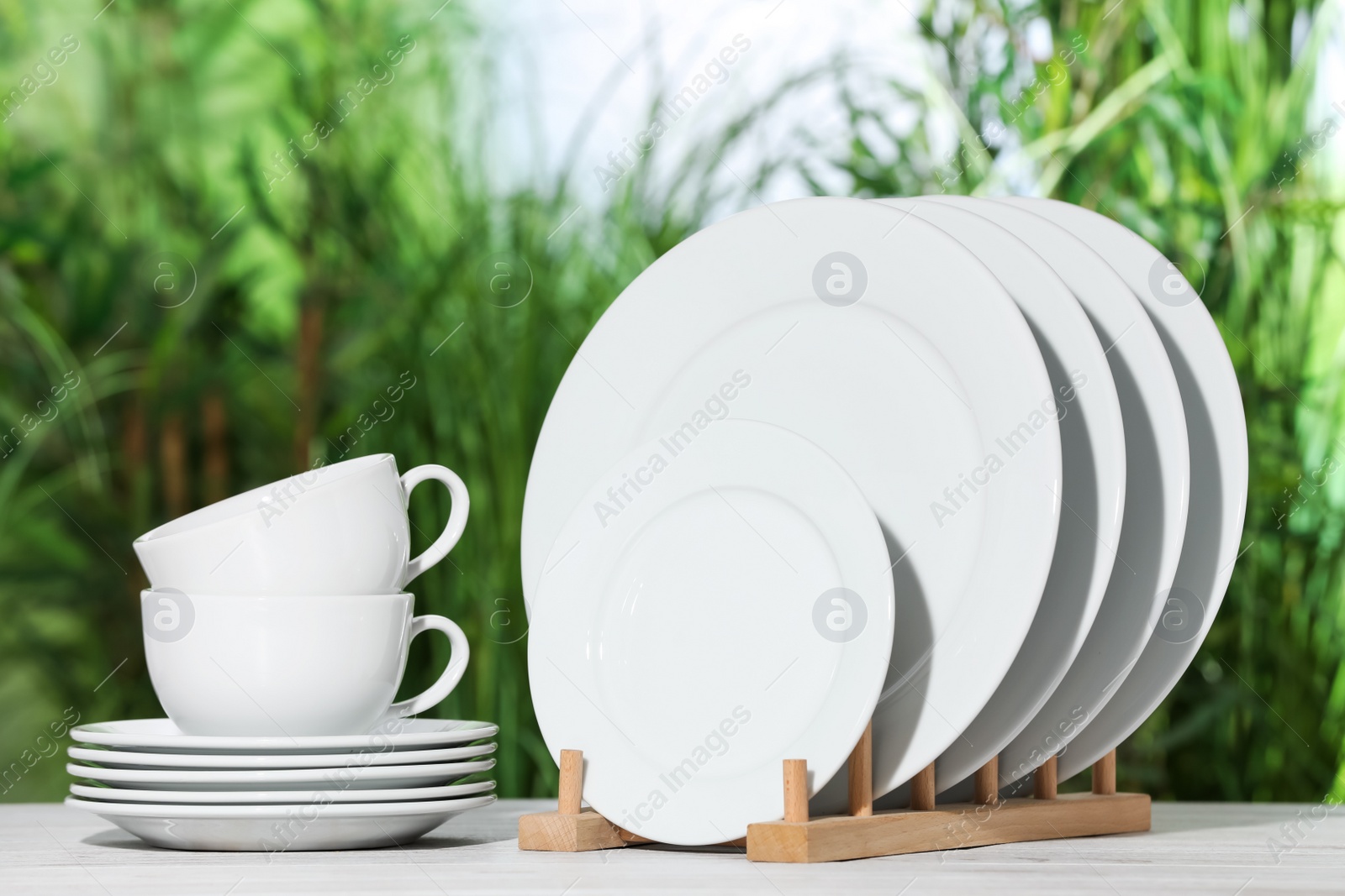 Photo of Set of clean dishware on white table against blurred background