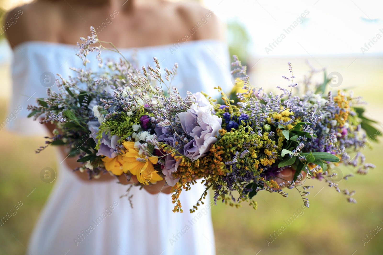 Photo of Young woman holding wreath made of beautiful flowers outdoors on sunny day, closeup