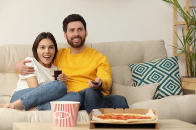 Photo of Happy couple watching TV with popcorn and pizza on sofa indoors, space for text