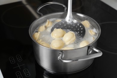 Photo of Cooking dumplings in saucepan with boiling water on cooktop, closeup