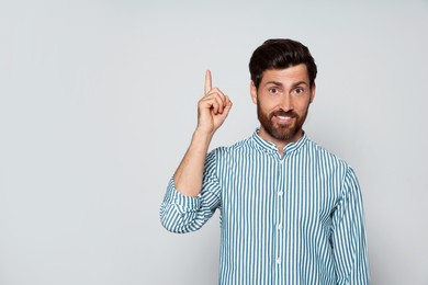 Bearded man pointing index finger up on grey background. Space for text