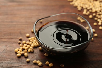 Soy sauce in bowl and soybeans on wooden table, closeup. Space for text