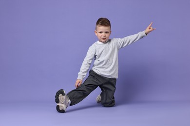Photo of Happy little boy dancing on violet background