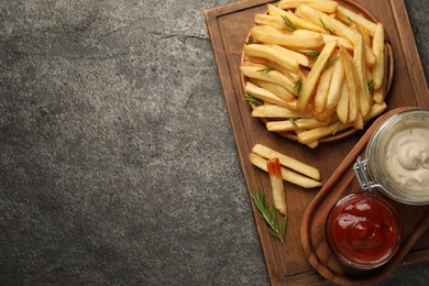 Delicious french fries served with sauces on grey textured table, top view. Space for text