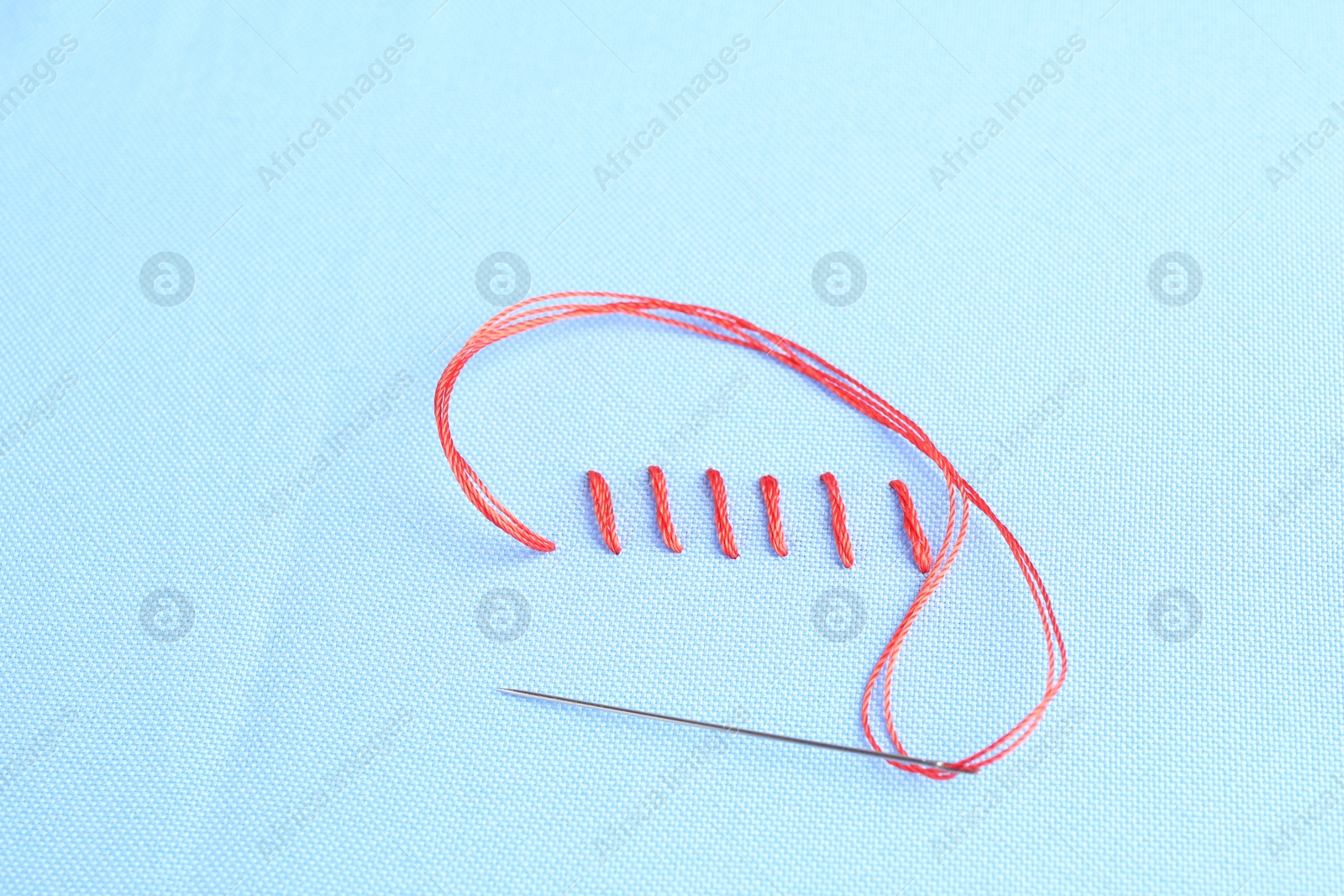 Photo of Sewing needle with thread and stitches on light blue cloth, above view